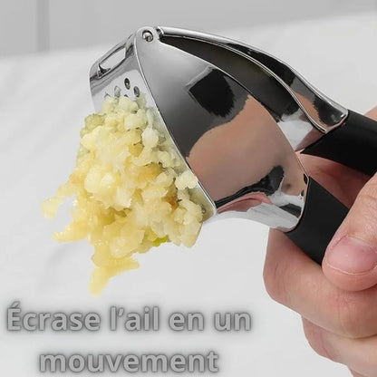 Presse A ail inox ergonomique avec poignées noires, posée sur une planche de cuisine en bois clair, ail fraîchement écrasé.