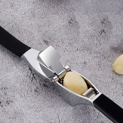 Presse A ail inox ergonomique avec poignées noires, posée sur une planche de cuisine en bois clair, ail fraîchement écrasé.