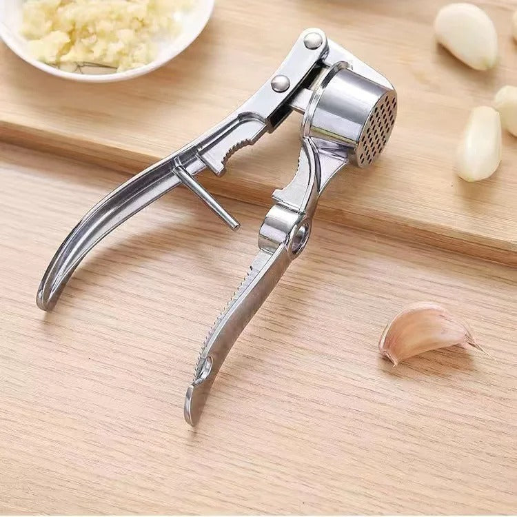 Presse-ail inox multifonction Titan 5 en 1 sur une planche de cuisine avec gousses d’ail